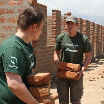 Projects Abroad teenage building volunteers working in Tanzania carry bricks needed to erect a wall. Teenage volunteers doing construction work in Tanzania carry bricks needed for a wall.